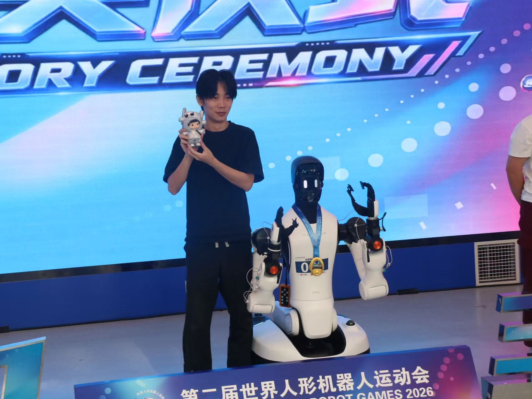 Wenhao Wang beside an AgiBot robot at the 2026 World Humanoid Robot Games award ceremony
